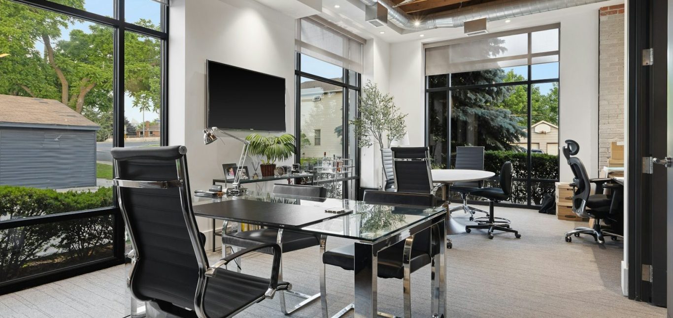 Modern office space with glass walls, multiple desks, and plenty of natural light.